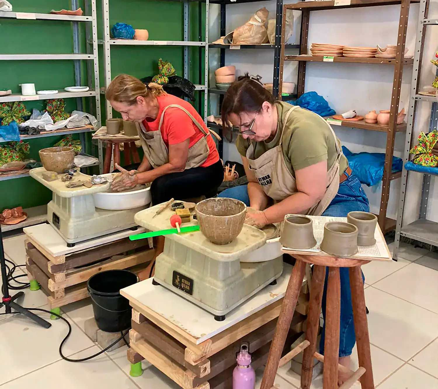 imagem de duas mulheres fazendo aulas de cerâmica utilizando o torno elétrico para modelar peças de argila
